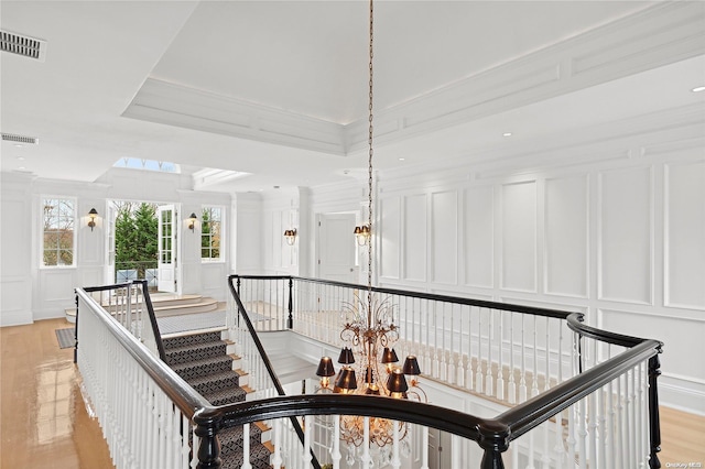 staircase featuring wood-type flooring, a raised ceiling, crown molding, and a notable chandelier