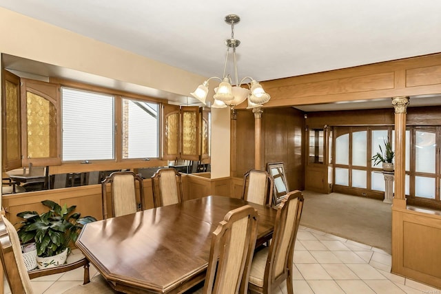 carpeted dining space featuring ornate columns, a notable chandelier, and wood walls