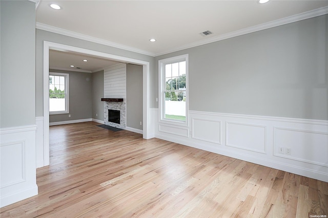 unfurnished living room with a stone fireplace, crown molding, plenty of natural light, and light hardwood / wood-style flooring