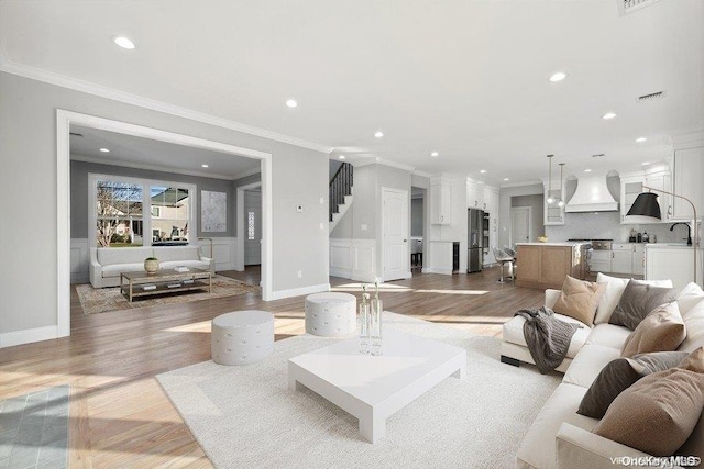 living room featuring sink, light wood-type flooring, and ornamental molding