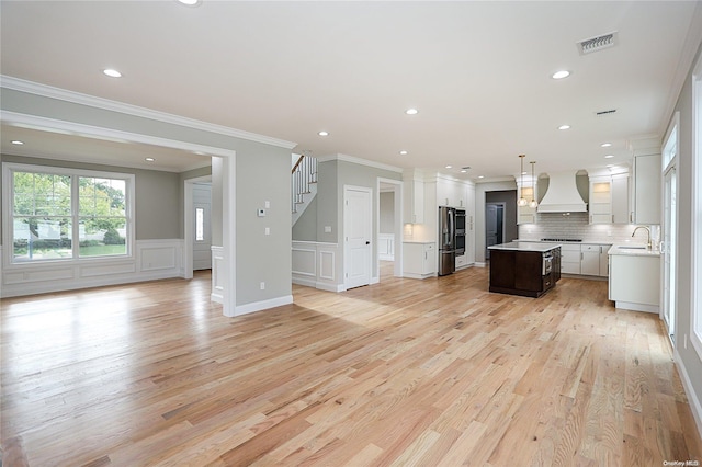 kitchen with premium range hood, sink, light hardwood / wood-style flooring, stainless steel fridge, and a kitchen island