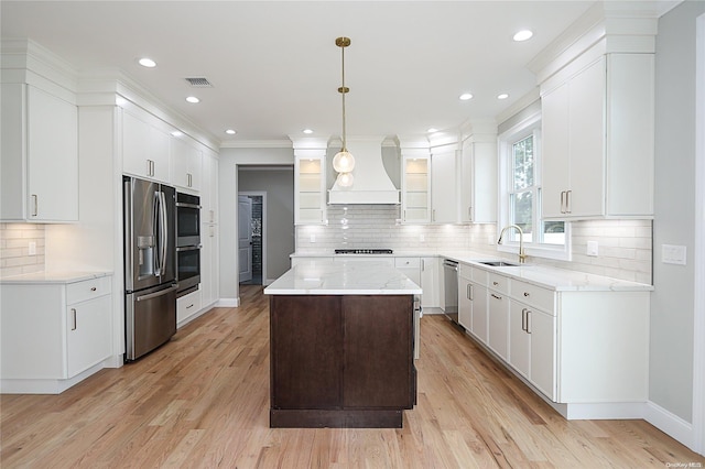 kitchen featuring premium range hood, hanging light fixtures, light wood-type flooring, appliances with stainless steel finishes, and a kitchen island