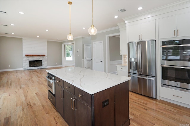 kitchen featuring appliances with stainless steel finishes, dark brown cabinets, a large fireplace, light hardwood / wood-style flooring, and white cabinets