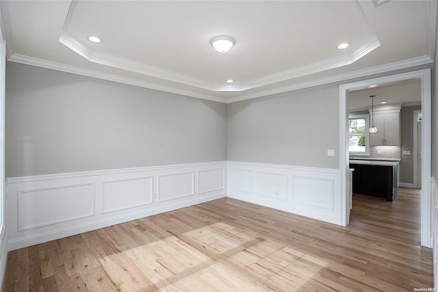 empty room featuring a raised ceiling, light wood-type flooring, and ornamental molding