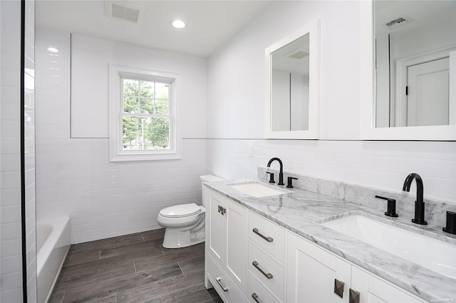 bathroom with vanity, a bath, hardwood / wood-style flooring, toilet, and tile walls