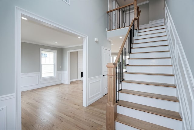 staircase with wainscoting, crown molding, wood finished floors, and recessed lighting