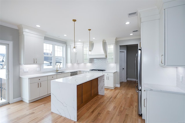 kitchen featuring crown molding, custom range hood, visible vents, a sink, and a kitchen island