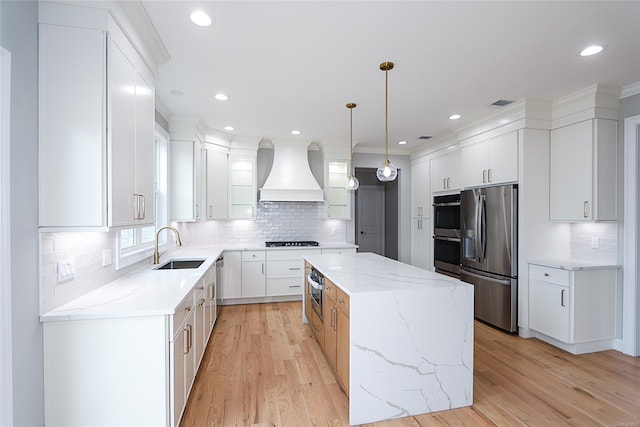 kitchen with a sink, a kitchen island, appliances with stainless steel finishes, light wood-type flooring, and custom exhaust hood