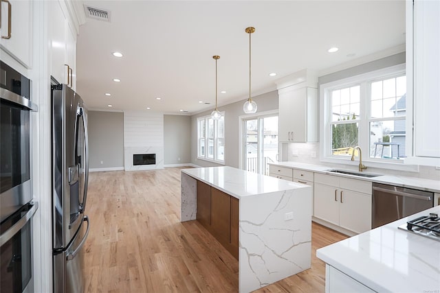 kitchen featuring visible vents, a kitchen island, a premium fireplace, stainless steel appliances, and a sink