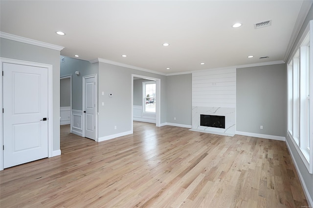 unfurnished living room featuring light wood-type flooring, a fireplace, visible vents, and ornamental molding