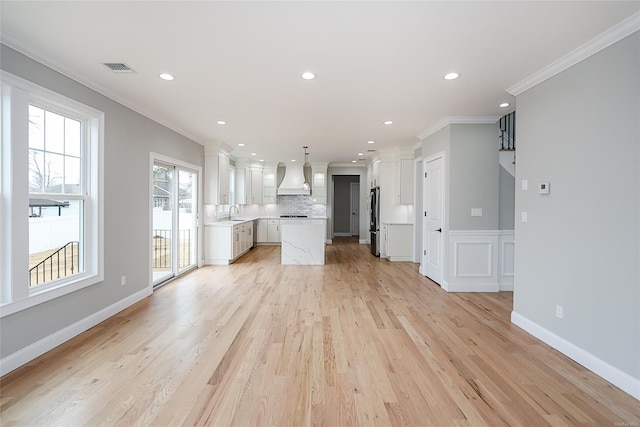 kitchen featuring tasteful backsplash, light countertops, ornamental molding, freestanding refrigerator, and premium range hood