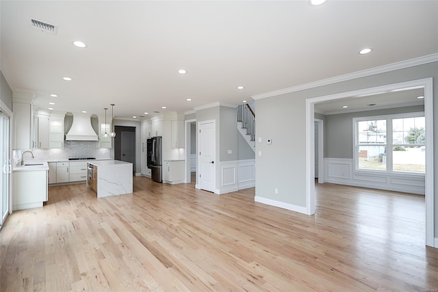 kitchen with light countertops, visible vents, freestanding refrigerator, a sink, and premium range hood