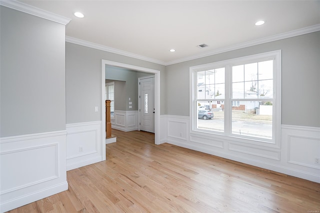 empty room featuring visible vents, a wainscoted wall, ornamental molding, light wood-type flooring, and recessed lighting