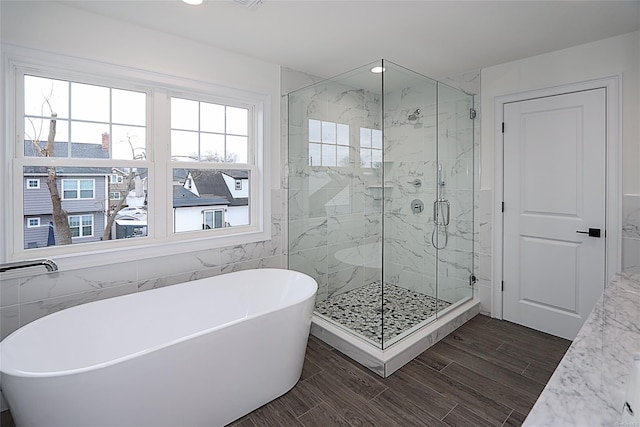 full bath with a soaking tub, a marble finish shower, tile walls, and wood finish floors