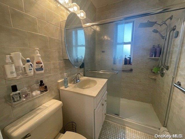 bathroom with backsplash, walk in shower, vanity, tile walls, and toilet