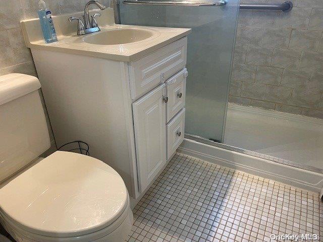 bathroom with tile patterned floors, toilet, a shower with door, vanity, and tile walls