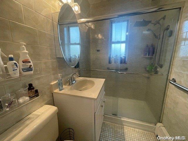 bathroom with vanity, a shower with door, backsplash, toilet, and tile walls