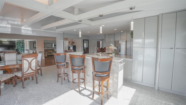 kitchen featuring stainless steel fridge, gray cabinetry, decorative light fixtures, beamed ceiling, and a breakfast bar area