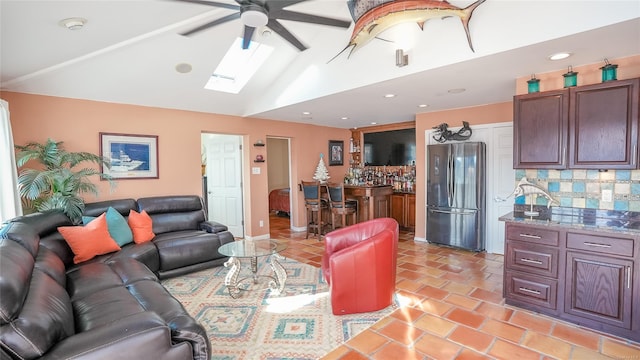 living room featuring vaulted ceiling with skylight, ceiling fan, light tile patterned floors, and indoor bar