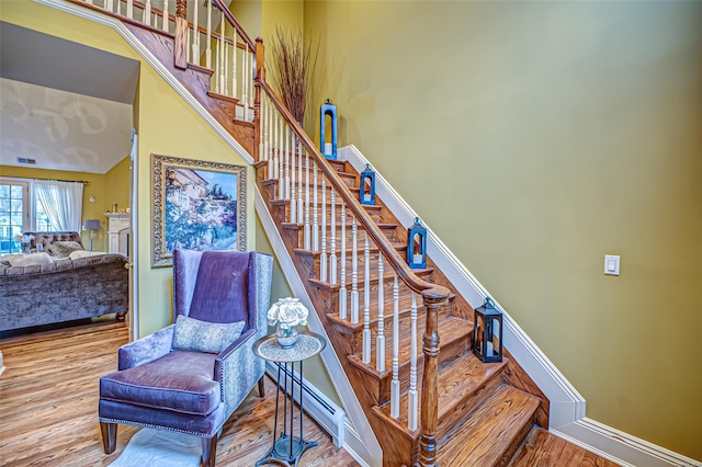 stairs with a baseboard radiator, a high ceiling, and hardwood / wood-style flooring