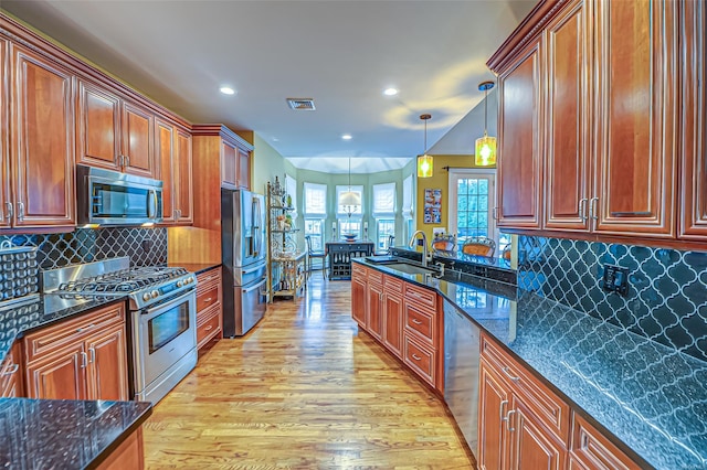 kitchen with sink, hanging light fixtures, light wood-type flooring, appliances with stainless steel finishes, and tasteful backsplash