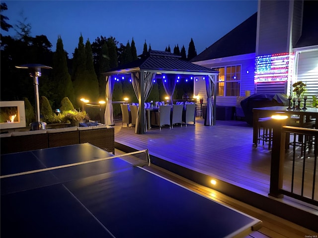 patio at twilight with a gazebo, a wooden deck, area for grilling, and an outdoor bar