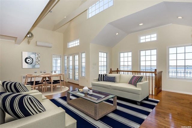 living room with a wall mounted air conditioner, a towering ceiling, hardwood / wood-style flooring, and a water view