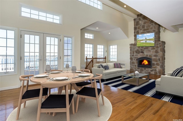 dining room featuring a stone fireplace, wood-type flooring, and a towering ceiling