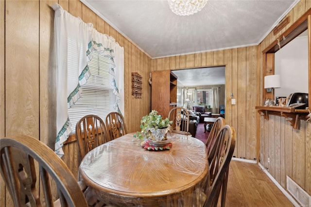 dining area with wood-type flooring, wooden walls, and ornamental molding