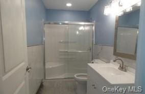 bathroom with a shower, vanity, toilet, and tile walls