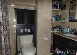 bathroom with a shower with curtain, vanity, toilet, and tile walls