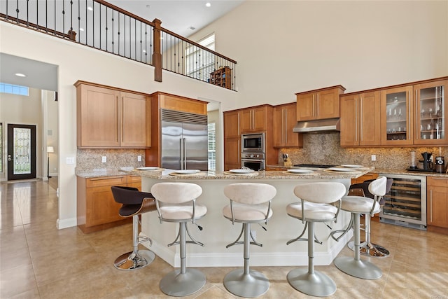 kitchen featuring built in appliances, light stone counters, beverage cooler, and a high ceiling