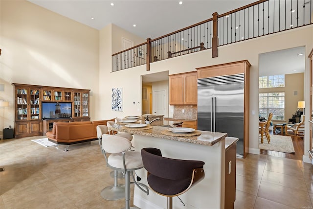 kitchen with light stone countertops, a kitchen bar, tasteful backsplash, a high ceiling, and built in refrigerator