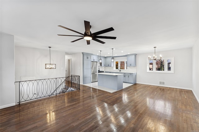 unfurnished living room featuring ceiling fan with notable chandelier and dark wood-type flooring