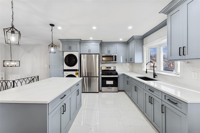 kitchen featuring appliances with stainless steel finishes, sink, pendant lighting, gray cabinets, and stacked washer / drying machine