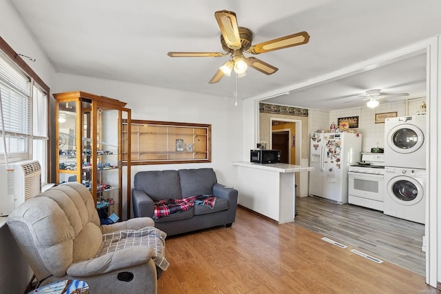 living room featuring ceiling fan, stacked washer / dryer, and light hardwood / wood-style floors