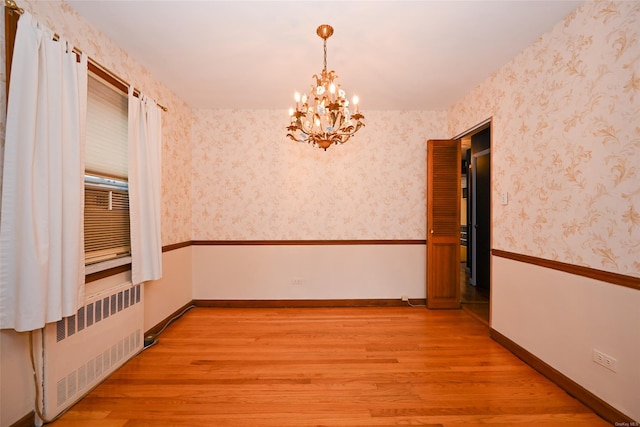 empty room featuring radiator heating unit, a chandelier, and light wood-type flooring