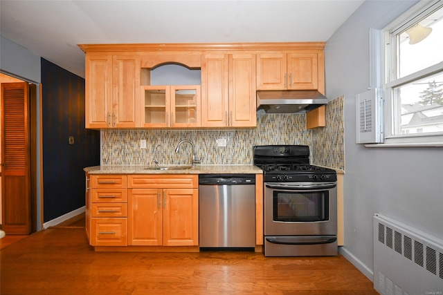 kitchen with sink, radiator heating unit, light stone counters, exhaust hood, and appliances with stainless steel finishes