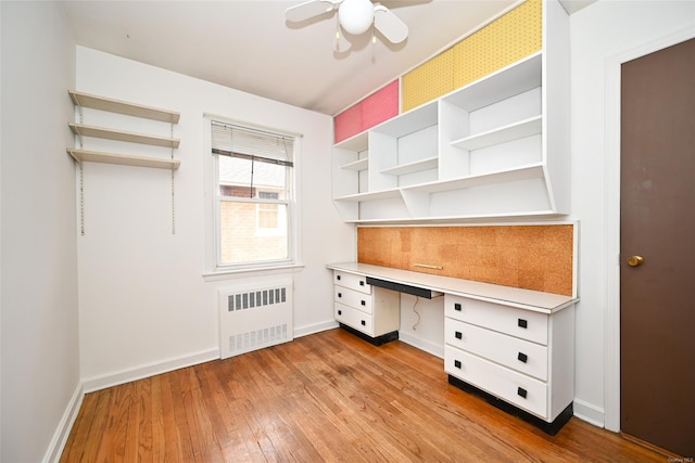 unfurnished office with radiator, ceiling fan, light hardwood / wood-style flooring, and built in desk