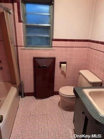 bathroom with a bathtub, vanity, tile patterned flooring, toilet, and tile walls