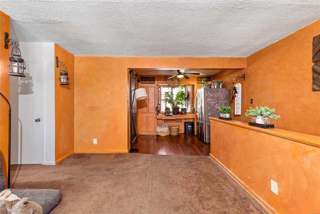 interior space with a textured ceiling, ceiling fan, and dark colored carpet