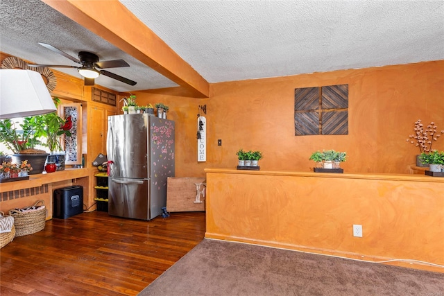 kitchen featuring dark wood-type flooring, stainless steel fridge, ceiling fan, beam ceiling, and a textured ceiling