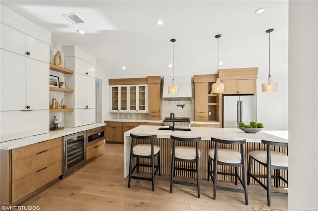 kitchen featuring stainless steel appliances, light hardwood / wood-style flooring, white cabinets, wine cooler, and an island with sink