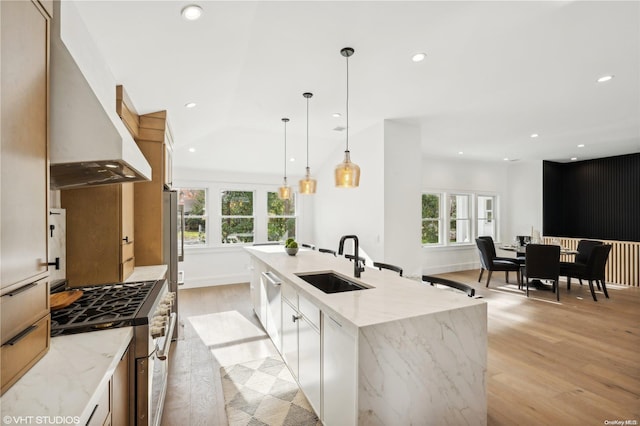 kitchen featuring a healthy amount of sunlight, wall chimney exhaust hood, a large island, and sink