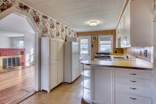 kitchen featuring stove, sink, white refrigerator, a fireplace, and white cabinetry