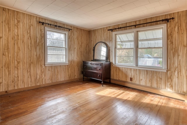 empty room with hardwood / wood-style floors, a baseboard heating unit, and wood walls