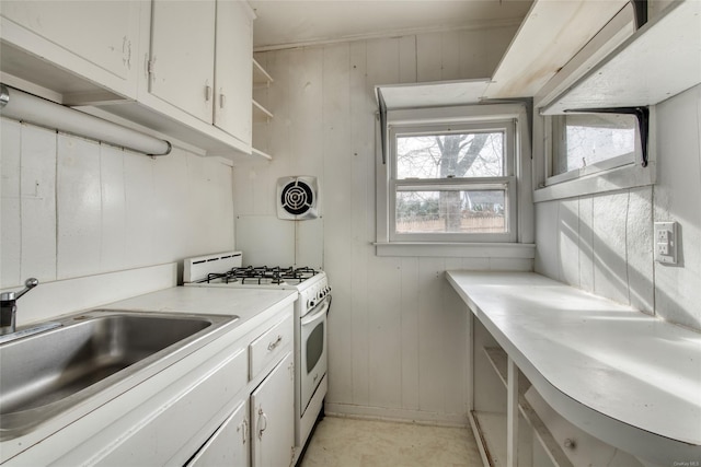 kitchen with white cabinetry, sink, white range with gas stovetop, and wooden walls