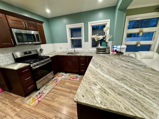 kitchen featuring light stone countertops, sink, stainless steel appliances, backsplash, and light hardwood / wood-style floors