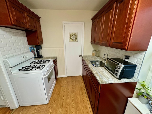 kitchen with sink, tasteful backsplash, light stone counters, white stove, and light wood-type flooring