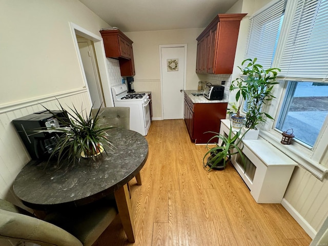 kitchen with decorative backsplash, white range with gas stovetop, wooden walls, and light hardwood / wood-style flooring